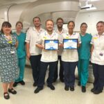 Team members stand together holding two certificates.