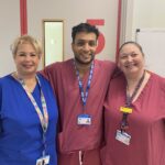 Three people standing side-by-side in NHS scrubs smiling.