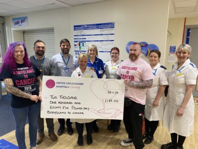 A group of people - nurses wearing uniforms and wrestlers presenting a cheque