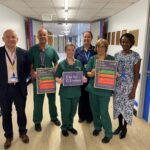 A group of six people stand in a hospital corridor holding up some posters with information on about the Call For Concern service.