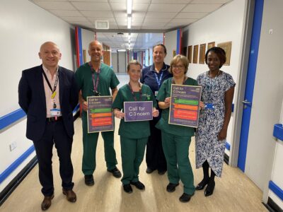 A group of six people stand in a hospital corridor holding up some posters with information on about the Call For Concern service.