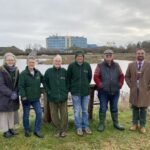 Boston Woods Trust Trustee Claire Elwood, Secretary Frances Brooks, President Adrian Isaac, Chairman Steve Elwood and Volunteer Simon Horniblow with United Lincolnshire Hospitals Charity Manager Ben Petts. They are stood on the edge of the lake with Pilgrim hospital in the background.